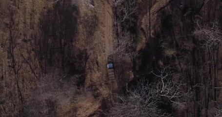 Aerial view of a lone vehicle driving along a dirt road cutting through a dense forest of leafless trees, creating a stark contrast, Lugenda, Niassa Province, Mozambique.