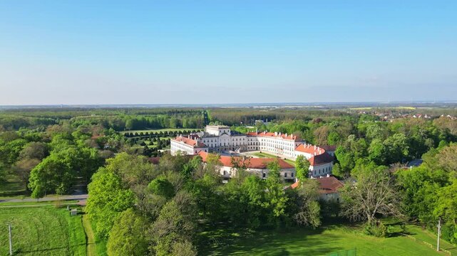 Aerial view of Esterhazy Castle surrounded by a vibrant green forest, the white walls contrasting against the orange rooftops, Fertod, Sopron, Hungary.