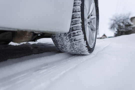 Low-angle view of a car tire gripping a snow-covered road. This perspective emphasizes vehicle stability, traction performance, and the importance of winter tires for safe seasonal commuting.