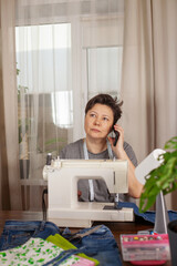 The woman behind the sewing machine sews a bag of old denim. Seamstress on the phone. Zero waste, hobby concept