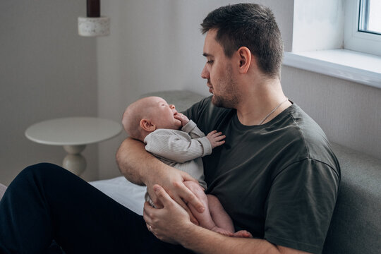A father comforts his crying little son. A man cradles his newborn in his arms. The concept of active fatherhood and love for the baby.