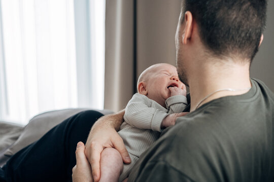 A father comforts his crying little son. A man cradles his newborn in his arms. The concept of active fatherhood and love for the baby.