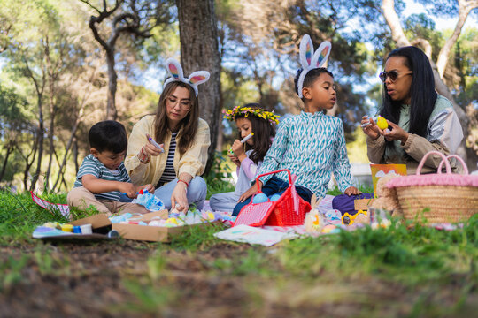 Multi ethnic family and friends enjoying easter picnic, decorating eggs and wearing bunny ears