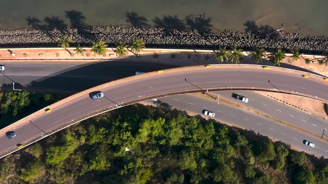 Aerial view of cars moving along the winding coastal road with contrasting green vegetation and blue water, Maputo, Mozambique.