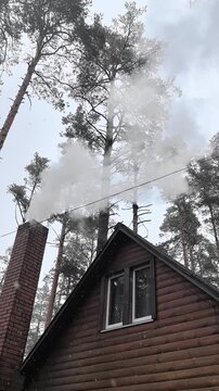 A lovely cabin nestled in a snowy forest lets out soft smoke from its chimney. Snowflakes dance through the air, creating a magical winter atmosphere around the warm abode.