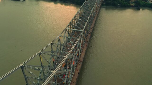 Aerial view of the majestic Howrah Bridge spanning the river, its steel structure contrasting with the water, a testament to engineering, Howrah, West Bengal, India.