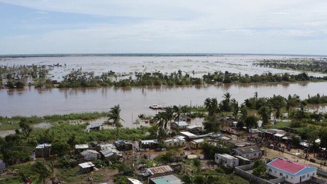 Aerial view of a muddy river cutting through a flooded landscape with damaged buildings, contrasting the murky water with the scattered green vegetation, Beira, Sofala Province, Mozambique.