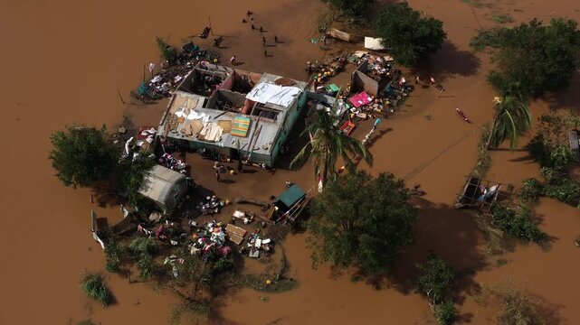 Aerial view of houses submerged in muddy floodwaters, contrasting with the green trees and scattered belongings, Beira, Sofala Province, Mozambique.