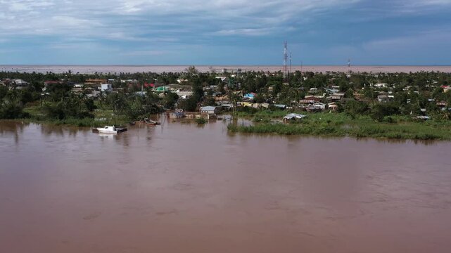 Aerial view of submerged houses and roads amidst brown floodwaters reflecting the cloudy sky, creating a somber landscape, Beira, Sofala Province, Mozambique.