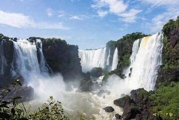 Fototapeta premium Majestic waterfalls cascading into a turbulent river under a blue sky