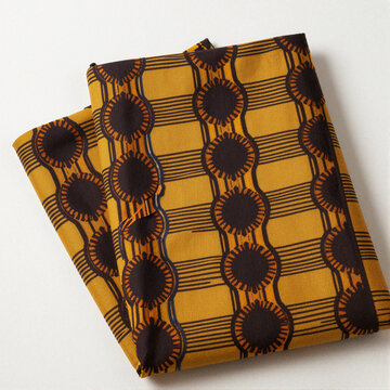 Bold Yoruba iro and buba fabric in mustard yellow with dark brown circular motifs and linear grid pattern, folded and centered on white
