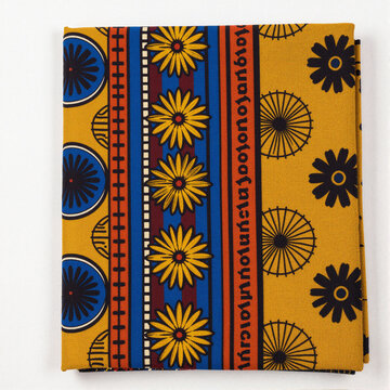 Bold Yoruba iro and buba fabric folded and centered on white, vibrant yellow wax print with sunflower and wheel motifs in blue, red, and orange