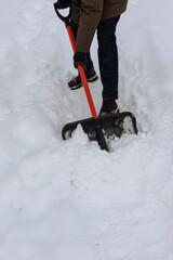 Man clearing sidewalk from snow with shovel outdoors. Winter shoveling snowdrifts after snowfall closeup.