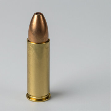 Shotgun slug with a round lead core and smooth outer copper shell standing upright on a white background