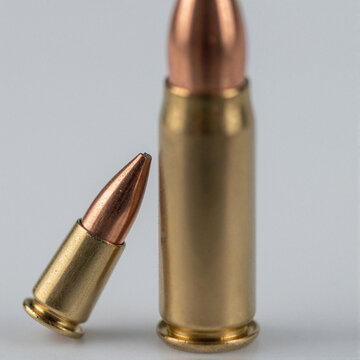 Macro close-up of a copper-jacketed rifle bullet tip with rifling marks, next to a brass cartridge, isolated on white