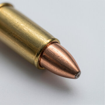 Macro close-up of a copper-jacketed bullet tip with rifling marks beside a brass cartridge on a white background