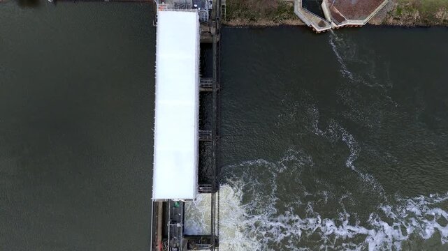 Aerial view of Colwick Sluice, where water flows powerfully over the structure, creating a stark contrast with the surrounding calm waters, Colwick, Nottingham, United Kingdom.