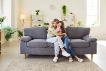 Obraz premium Mother and daughter hug with warm affection. Close view on a sofa at home shows family bonding, smile, and relationship in living room. Mom hugging with child. Love, care and mothers day. 