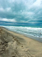 Fototapeta premium Footprints on a sandy beach near the ocean under a cloudy sky in a coastal area, a scene depicting nature and the shoreline during the day