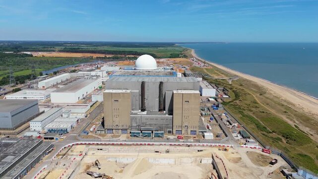 Aerial view of the Sizewell C nuclear power plant, contrasting its stark construction with the adjacent sandy beach and the vast expanse of the blue sea, Sizewell, England, United Kingdom.