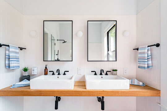 Modern double vanity bathroom with white vessel sinks, wood countertop and black fixtures in bright minimalist interior - Powered by Adobe