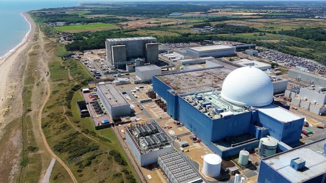 Aerial view of Sizewell C nuclear power plant with stark blue buildings and a white dome contrasting against the sandy coast, Sizewell, England, United Kingdom.