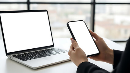 Person using smartphone and laptop with blank screens in modern office
