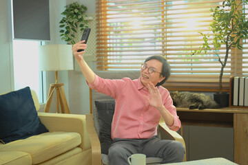 Senior man smiling and waving during a video call on smartphone at home, enjoying digital communication