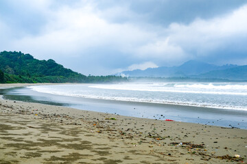 Cloudy atmosphere over Rajegwesi Beach in Banyuwangi features wide sandy shores, gentle waves, and forested hills, serving as a quiet coastal retreat and boat transit point to Green Bay. South Java.