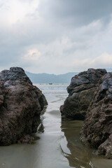 Rocky shoreline at Rajegwesi Beach inside Meru Betiri National Park, featuring coral rocks, calm waves, tropical forest backdrop, and overcast skies along the southern coast of Java.