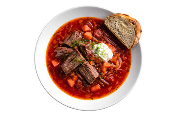 A bowl of red soup with meat and carrots sits on a white plate