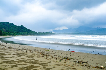Cloudy atmosphere over Rajegwesi Beach in Banyuwangi features wide sandy shores, gentle waves, and forested hills, serving as a quiet coastal retreat and boat transit point to Green Bay. South Java.