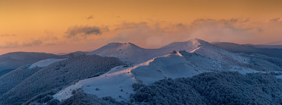 Legendary Chatka Puchatka on Połonina Wetlińska illuminated by warm golden sunset light in winter conditions. Iconic view of the Bieszczady Mountains seen from Połonina Caryńska, showing dramatic cont
