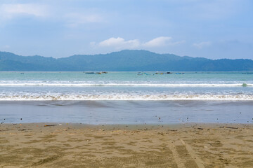 Cloudy atmosphere over Rajegwesi Beach in Banyuwangi features wide sandy shores, gentle waves, and forested hills, serving as a quiet coastal retreat and boat transit point to Green Bay. South Java.