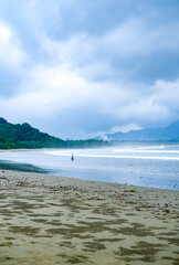 Cloudy atmosphere over Rajegwesi Beach in Banyuwangi features wide sandy shores, gentle waves, and forested hills, serving as a quiet coastal retreat and boat transit point to Green Bay. South Java.