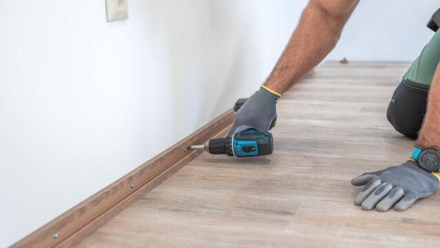 Installing elegant plastic baseboard, showcasing skilled craftsmanship in home improvement and renovation. Worker using a screwdriver to mount skirting board, plinth.