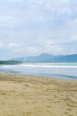 Cloudy atmosphere over Rajegwesi Beach in Banyuwangi features wide sandy shores, gentle waves, and forested hills, serving as a quiet coastal retreat and boat transit point to Green Bay. South Java.
