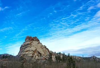 Massive granite dome rising from high plains forest at Vedauwoo Recreation Area in Wyoming beneath sweeping blue sky with wispy clouds showcasing rugged geology