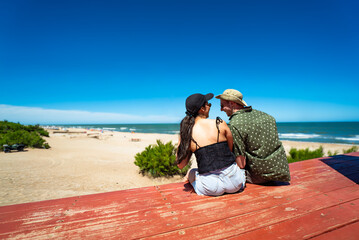 A man and a woman are sitting on a red bench on a beach