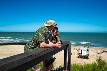 A man and a woman are sitting on a wooden platform overlooking the beach