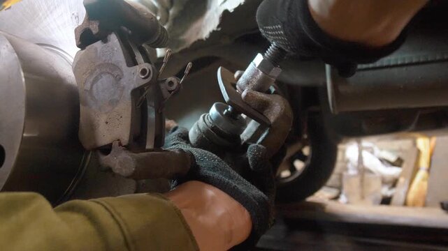 Professional auto mechanic in gloves using a special tool to press in a rear caliper piston for new brake pad installation, performing car maintenance and repair in a workshop garage