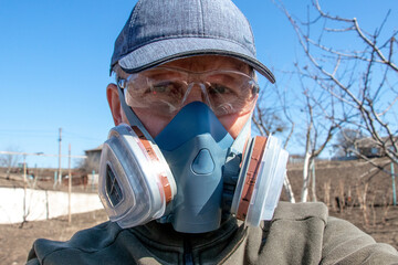 Man in respirator and safety goggles in backyard, worker in personal protective equipment outdoors