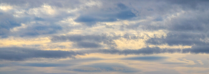 Scenic panoramic sky with layered gray clouds and golden sunlight peeking through the clouds during sunrise or sunset