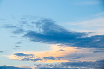 Fototapeta premium Bright blue sky with delicate clouds and warm golden-pink hues at sunset