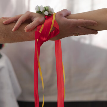 Close-up detail of wedding handfasting ritual with bride and groom hands tied by a red ribbon. Clean background, soft light and strong symbolic meaning of unity and commitment.