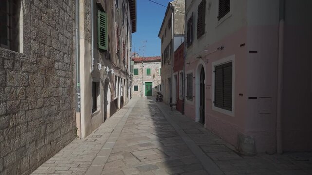 POV walking along an alley between historic mediterranean houses made of time-worn stones. Real time old town street view, sunny summer afternoon in Porec, Croatia.