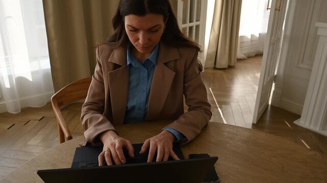Confident young professional woman working remotely from her home office, intently typing on a laptop keyboard and managing her business tasks with concentration and a serious expression
