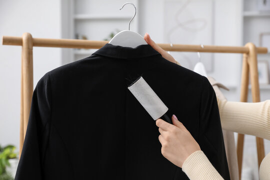 Woman cleaning jacket with lint roller at home, closeup