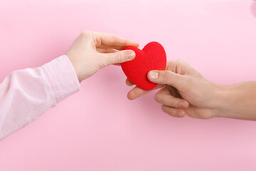 People with red decorative heart on pink background, top view