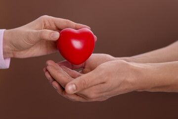 Woman giving red decorative heart to man on brown background, closeup